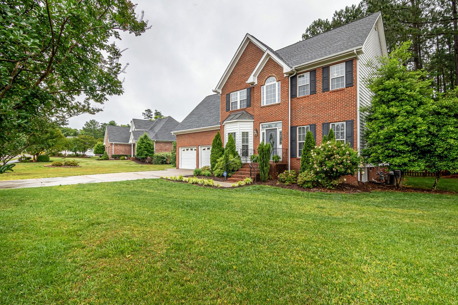 Two-story brick home with a manicured front lawn and mature trees